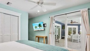 Camera da letto con un letto, una ventola a soffitto, un quadro e vista su uno spazio esterno attraverso una porta in vetro.