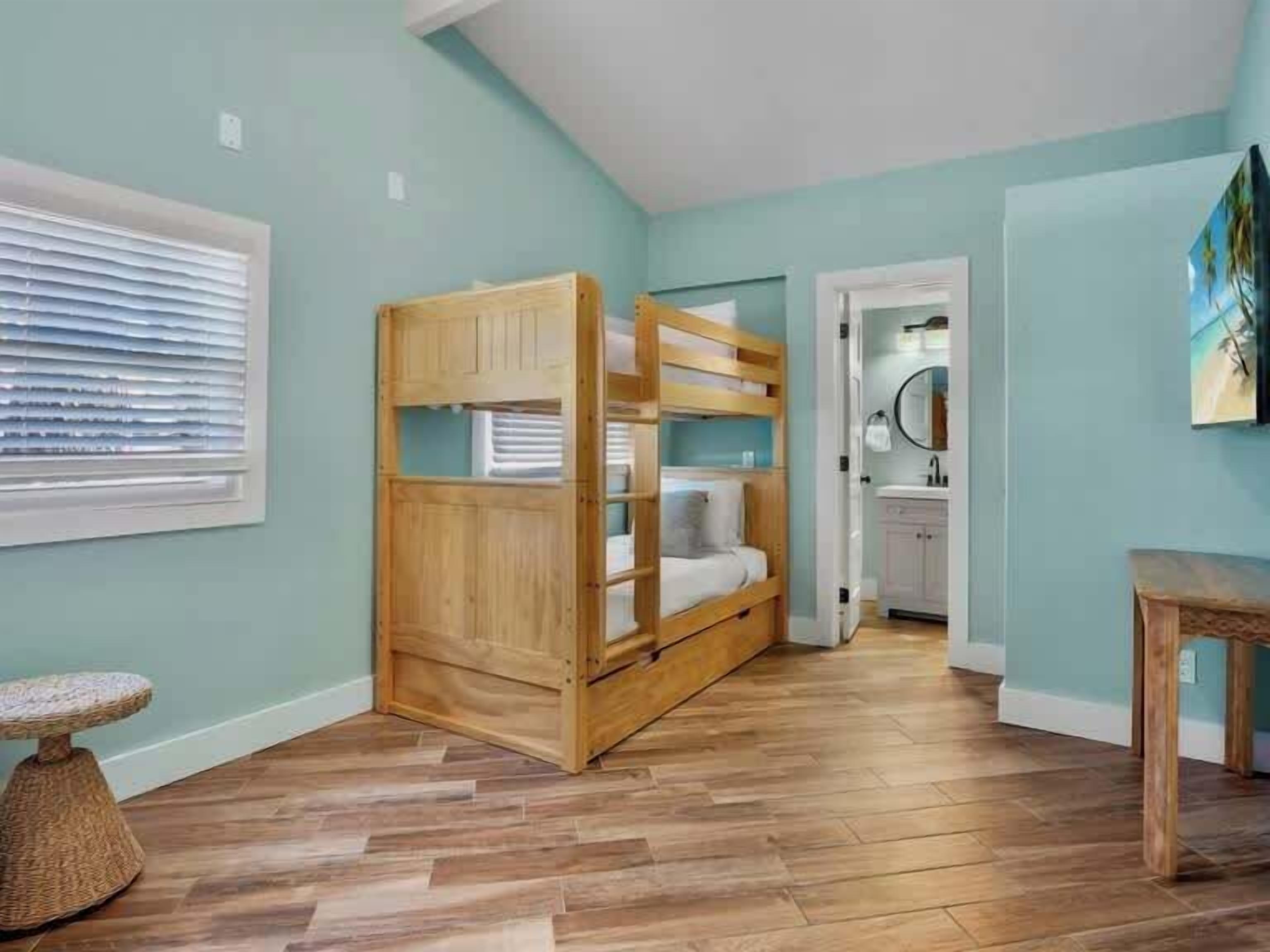 A room with a bunk bed, a small round table, a window with blinds, and a door leading to a bathroom.