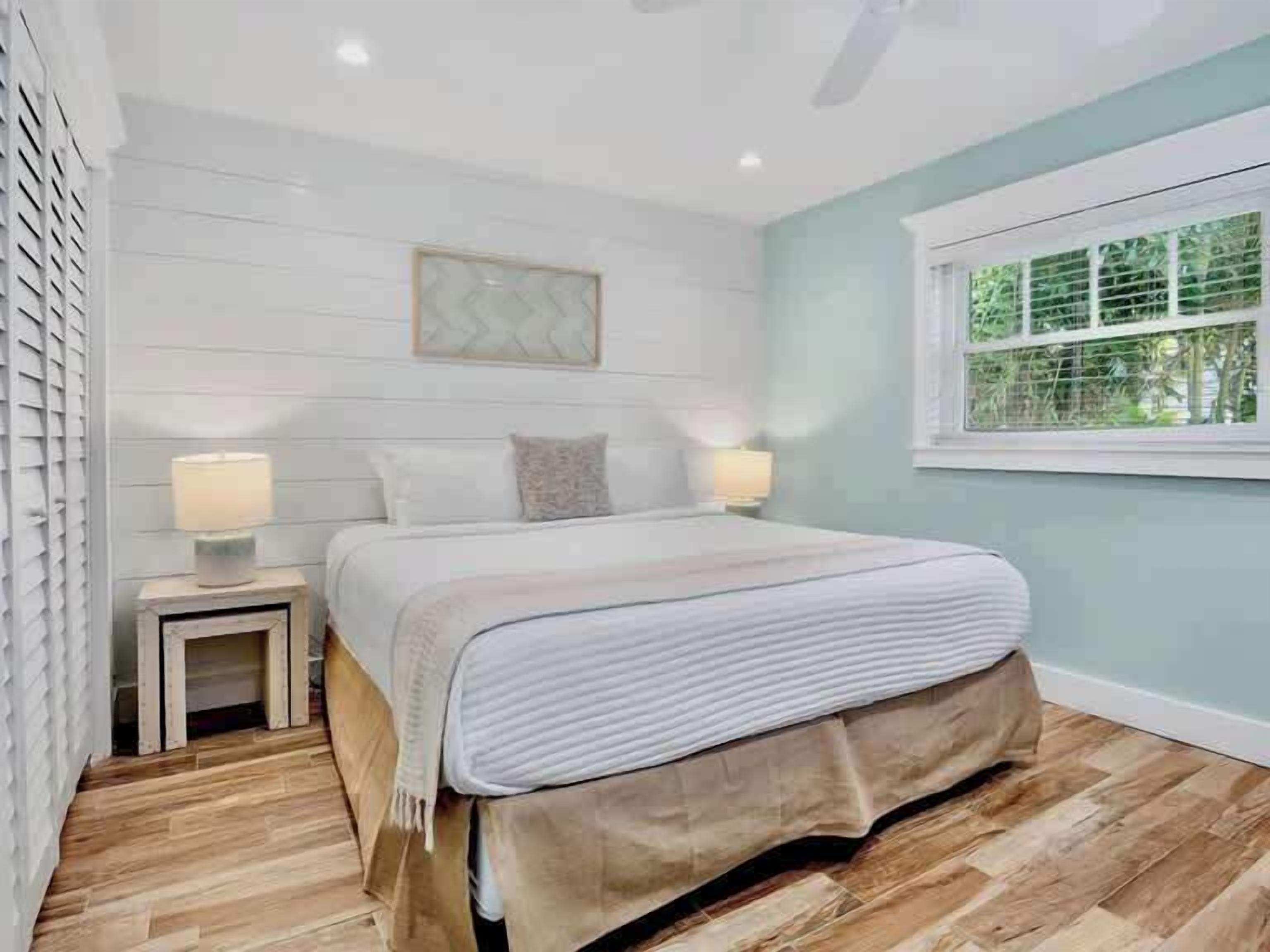 A bedroom with a bed, two bedside tables, a window with blinds, and a ceiling fan.