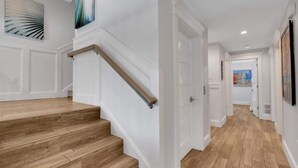 Een trap met houten treden en een leuning, witte muren en een deur die naar een andere kamer leidt.