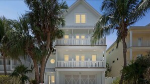 Een twee verdiepingen tellend strandpand met balkon, garage en palmbomen.