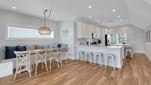 Een moderne keuken met witte kasten, een centraal eiland met krukken, en een eetgedeelte met een houten tafel en stoelen.