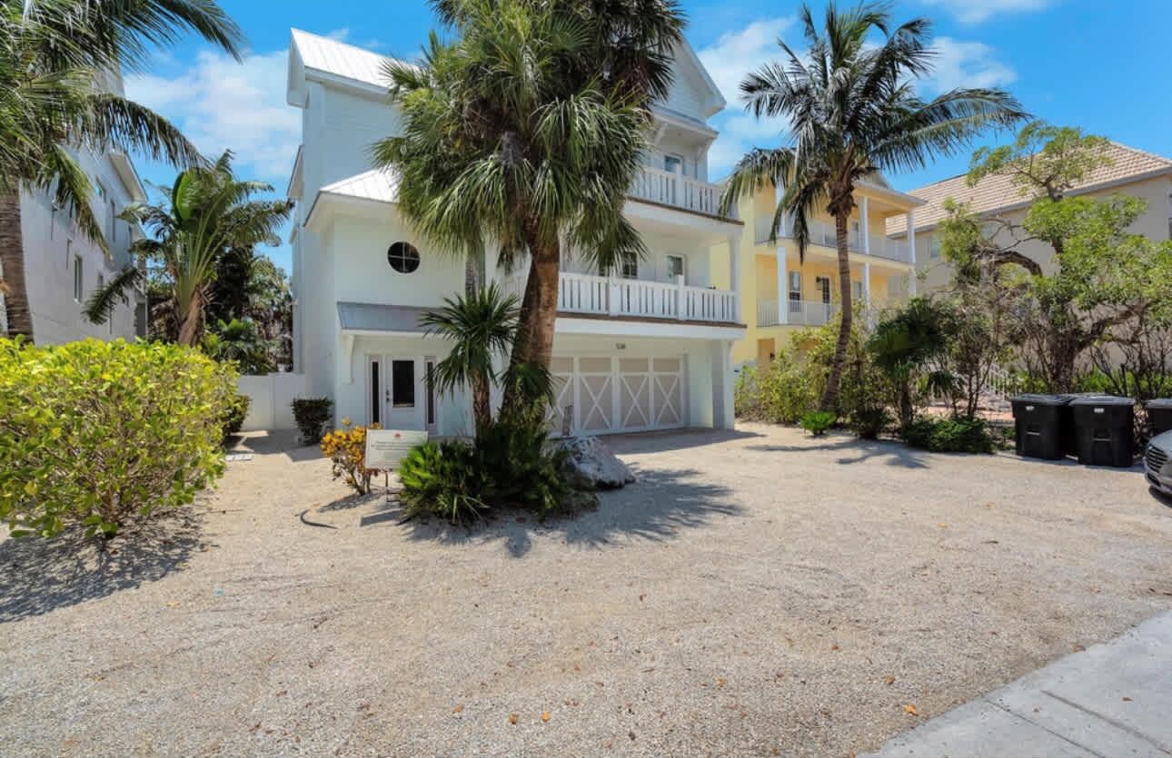 A two-story building with a white facade, a balcony on the second floor, and a gravel driveway.