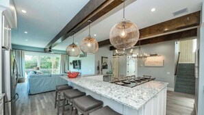 Une cuisine moderne dotée d’un grand îlot central, de luminaires suspendus et offrant une vue sur l’extérieur.
