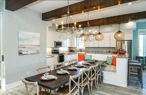 A modern kitchen with a dining area, wooden beams, pendant lights, and a view of the ocean. - Dry Dock | Canal-Front Retreat on Siesta Key (Siesta Key)
