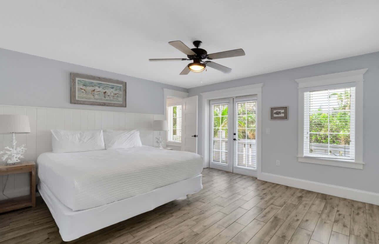 Une chambre à coucher comprenant un lit, un ventilateur de plafond, une table de chevet et une fenêtre avec des stores.