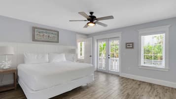 Une chambre à coucher comprenant un lit, un ventilateur de plafond, une table de chevet et une fenêtre avec des stores.