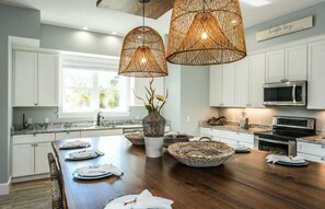 A modern kitchen with white cabinets, a wooden dining table, and wicker baskets. - Salty Dog | Siesta Key Canal-Front Escape! (Siesta Key)