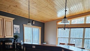 A kitchen with wooden cabinets, a large island with a sink, pendant lights, and windows with a snowy view. - Oasis in Saginaw - Pvt Pool, Hot Tub (Saginaw)