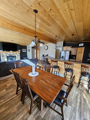 Une cuisine spacieuse avec des meubles en bois, un coin repas doté d’une grande table et de chaises en bois, et un salon confortable avec une cheminée.