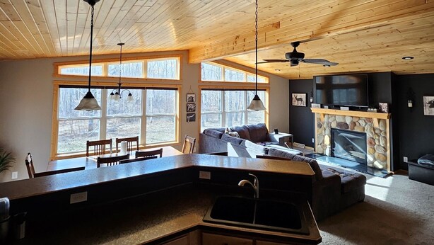 A spacious kitchen with wooden cabinets, a dining area with a table and chairs, and a living room with a sofa and fireplace. - Oasis in Saginaw - Pvt Pool, Hot Tub (Saginaw)