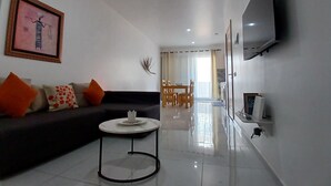 A modern living room with a sofa, a coffee table, a dining area with chairs and a table, a flat-screen TV mounted on the wall, and a framed artwork on the wall. - Charming apartment 2 minutes from Cabral Beach (Sal Rei)