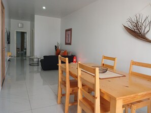 A dining area with a wooden table and chairs, a black sofa, a small round table, and a wall-mounted clock. - Charming apartment 2 minutes from Cabral Beach (Sal Rei)