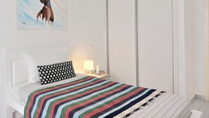 A bedroom with a bed, a pillow, a bedside table with a lamp, and a wall with a painting. - Charming apartment 2 minutes from Cabral Beach (Sal Rei)