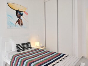 A bedroom with a bed, a pillow, a bedside table with a lamp, and a wall with a painting. - Charming apartment 2 minutes from Cabral Beach (Sal Rei)