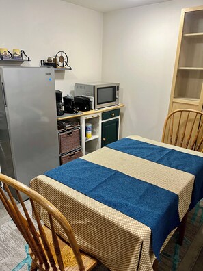 Een kleine kamer met een bed, een kitchenette, een koelkast en een houten stoel.