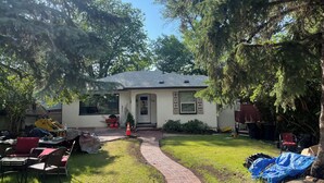 A house with a paved driveway leading to a front door, surrounded by trees and a grassy yard. - Enjoyable 2-bedroom Max 4 guests in lower level with AC in vibrant inner-city (Calgary)