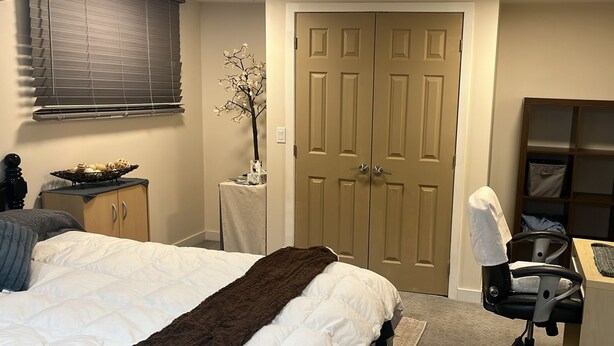 A bedroom with a bed, a desk, a chair, a wardrobe, and a door. - Enjoyable 2-bedroom Max 4 guests in lower level with AC in vibrant inner-city (Calgary)