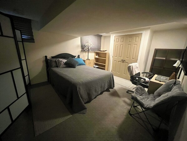 Een slaapkamer met een bed, een bureau, een stoel, een kledingkast en een raam met jaloezieën.