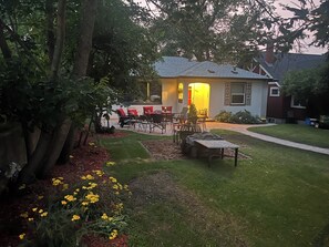 Een achtertuin met terras, tuinmeubilair en een huis met schoorsteen.