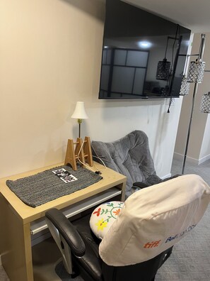 Un petit bureau comprenant un bureau, une chaise, une lampe et un téléviseur fixé au mur.