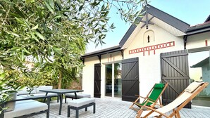 An outdoor patio with a table and chairs, a green folding chair, and a building with large black doors. - Renovated villa in the heart of Arcachon + outbuilding (Arcachon)