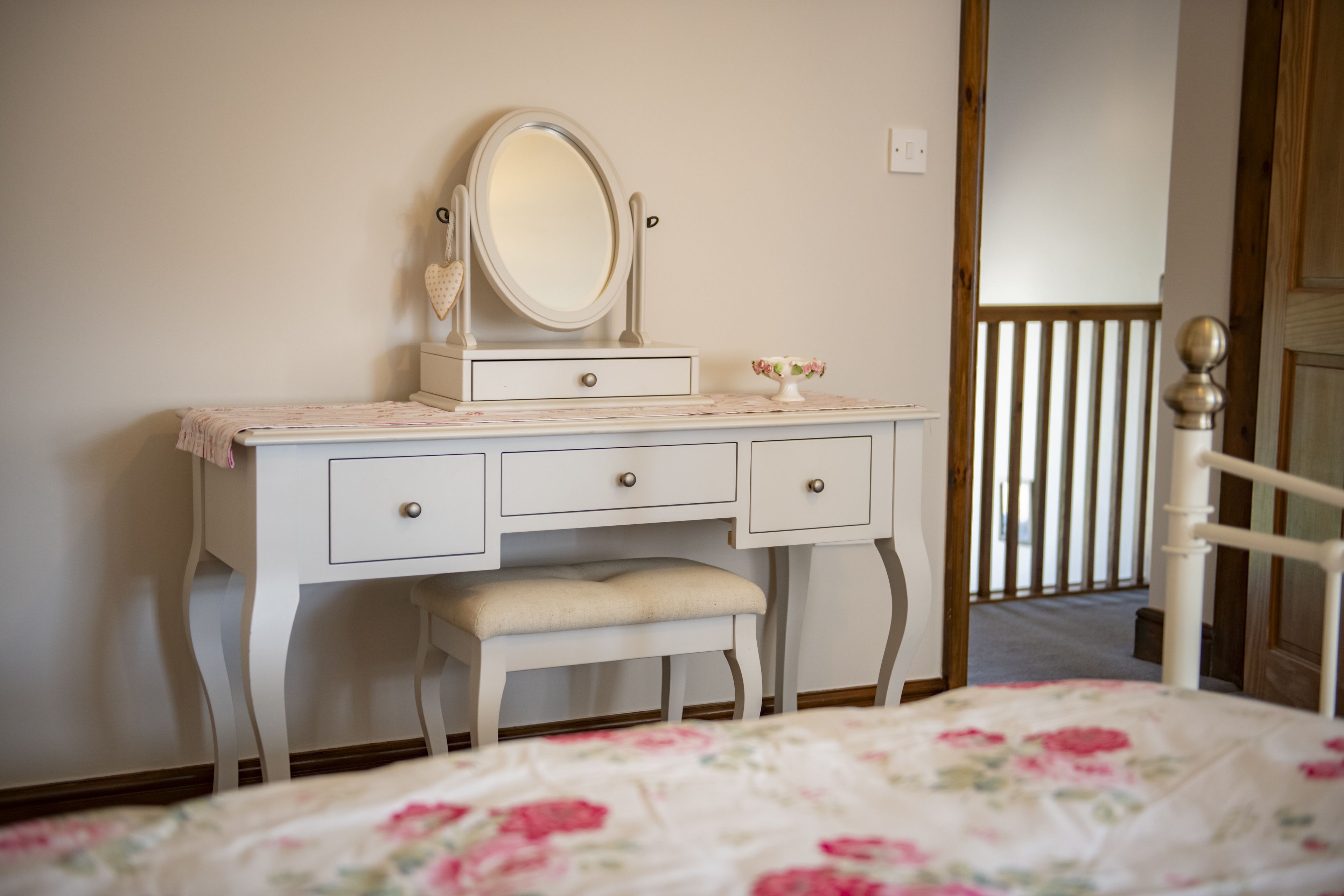 Une chambre à coucher avec un lit, une commode blanche à tiroirs, un banc, un miroir et un petit vase.