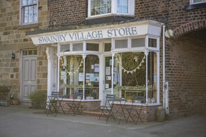 A brick building with a shop named 'Swanby Village Store' featuring large windows, a door, and outdoor seating. - Lyke Wake Cottage, Swainby, Yorkshire (Northallerton)
