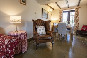 A room with a leather armchair, a round table with a checkered tablecloth, a dining table with chairs, and a window with curtains. - Lyke Wake Cottage, Swainby, Yorkshire (Northallerton)