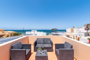 Eine Dachterrasse mit Gartenmöbeln, Solaranlagen und Blick auf das Meer.
