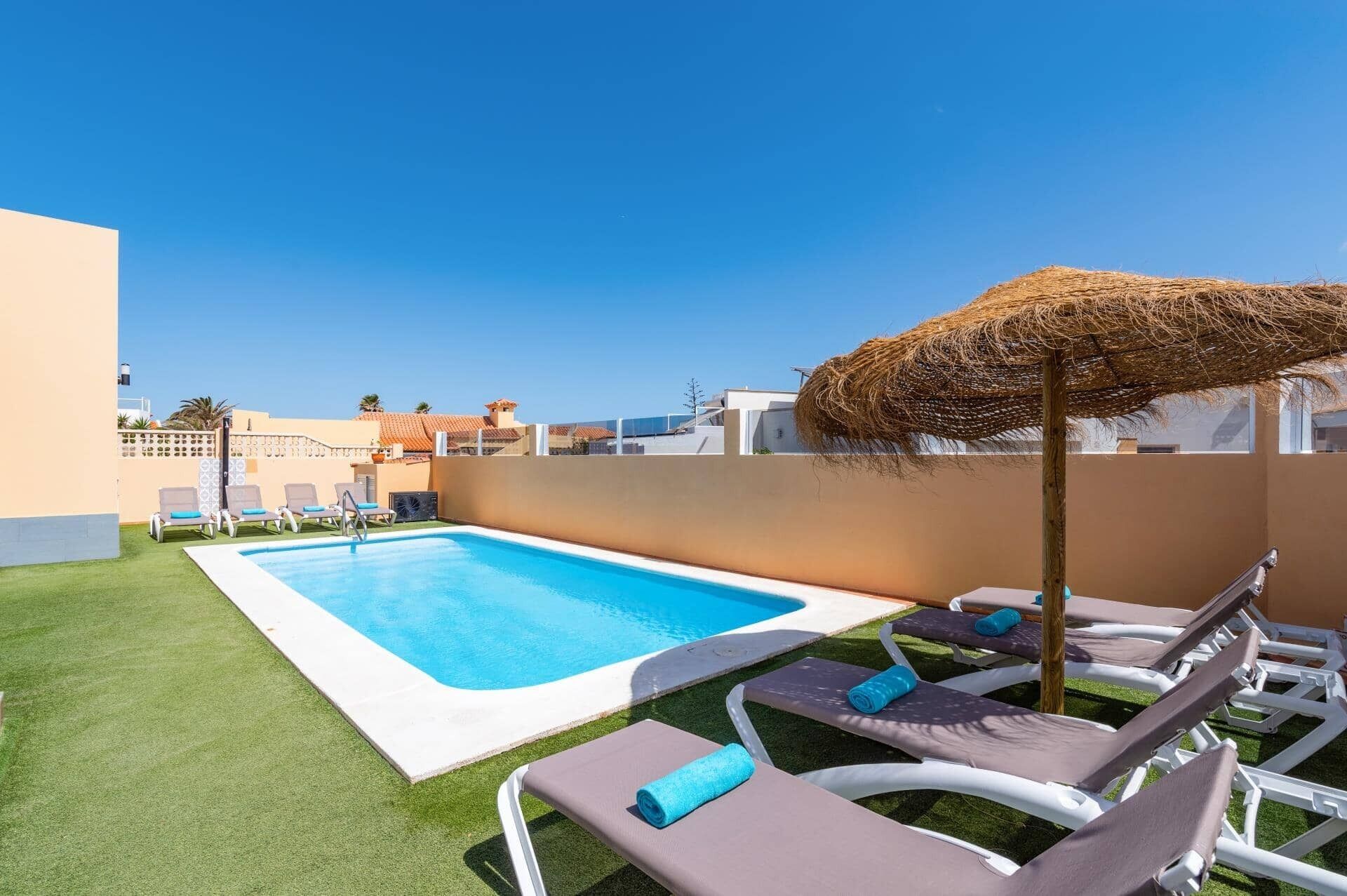 A swimming pool with lounge chairs and a straw umbrella.