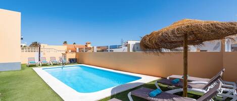 A swimming pool with lounge chairs and a straw umbrella.