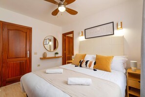 Ein Schlafzimmer mit einem Bett, einem Deckenventilator, einem gerahmten Bild, einem Nachttisch und einem Beistelltisch.