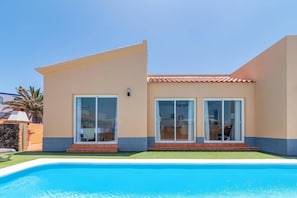 Ein modernes Haus mit Swimmingpool, großen Schiebeglasfenstern und einem Ziegeldach.