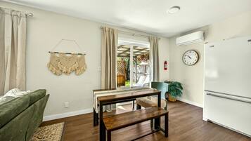 A living room with a sofa, a wooden table, a bench, a clock, and a refrigerator.