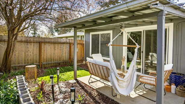 Un patio couvert avec un fauteuil suspendu, du mobilier d’extérieur et un espace jardin agrémenté d’un sentier en pierre.