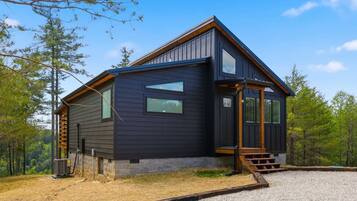 A modern cabin with a dark exterior, large windows, and a wooden staircase leading to the entrance.