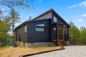 A modern cabin with a dark exterior, large windows, and a wooden staircase leading to the entrance.
