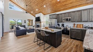 Una cocina moderna con una isla grande, armarios oscuros y techo de madera.