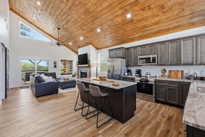 A modern kitchen with a large island, dark cabinetry, and a wooden ceiling.