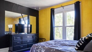A bedroom with a bed, a dresser, a television, and a window with curtains. - Retro 1BR Flat in the Heart of East Liberty | Queen Bed | Longer Stays Welcome (Pittsburgh)