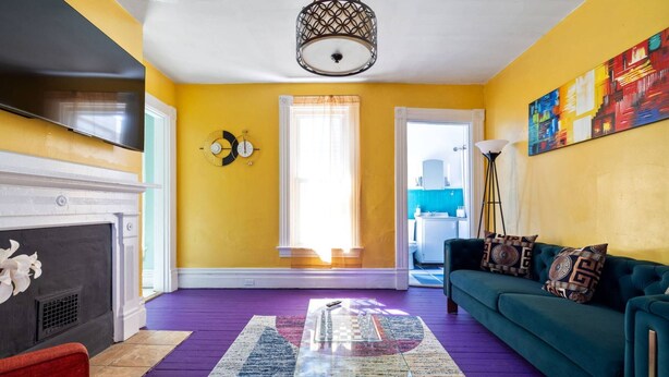 A living room with a fireplace, a sofa, a coffee table, and a large window with curtains. - Retro 1BR Flat in the Heart of East Liberty | Queen Bed | Longer Stays Welcome (Pittsburgh)
