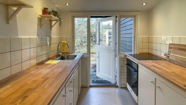 Une cuisine étroite avec des plans de travail en bois, un évier et une porte donnant sur l’extérieur.