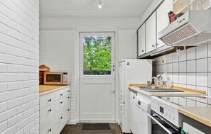 A compact kitchen with white brick walls, a microwave, a refrigerator, a stove, and a window with a view of trees. - 3 bedroom cozy home in Højby (Højby)