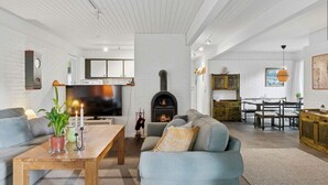 A modern living room with a fireplace, a dining area, and a kitchen with white brick walls.