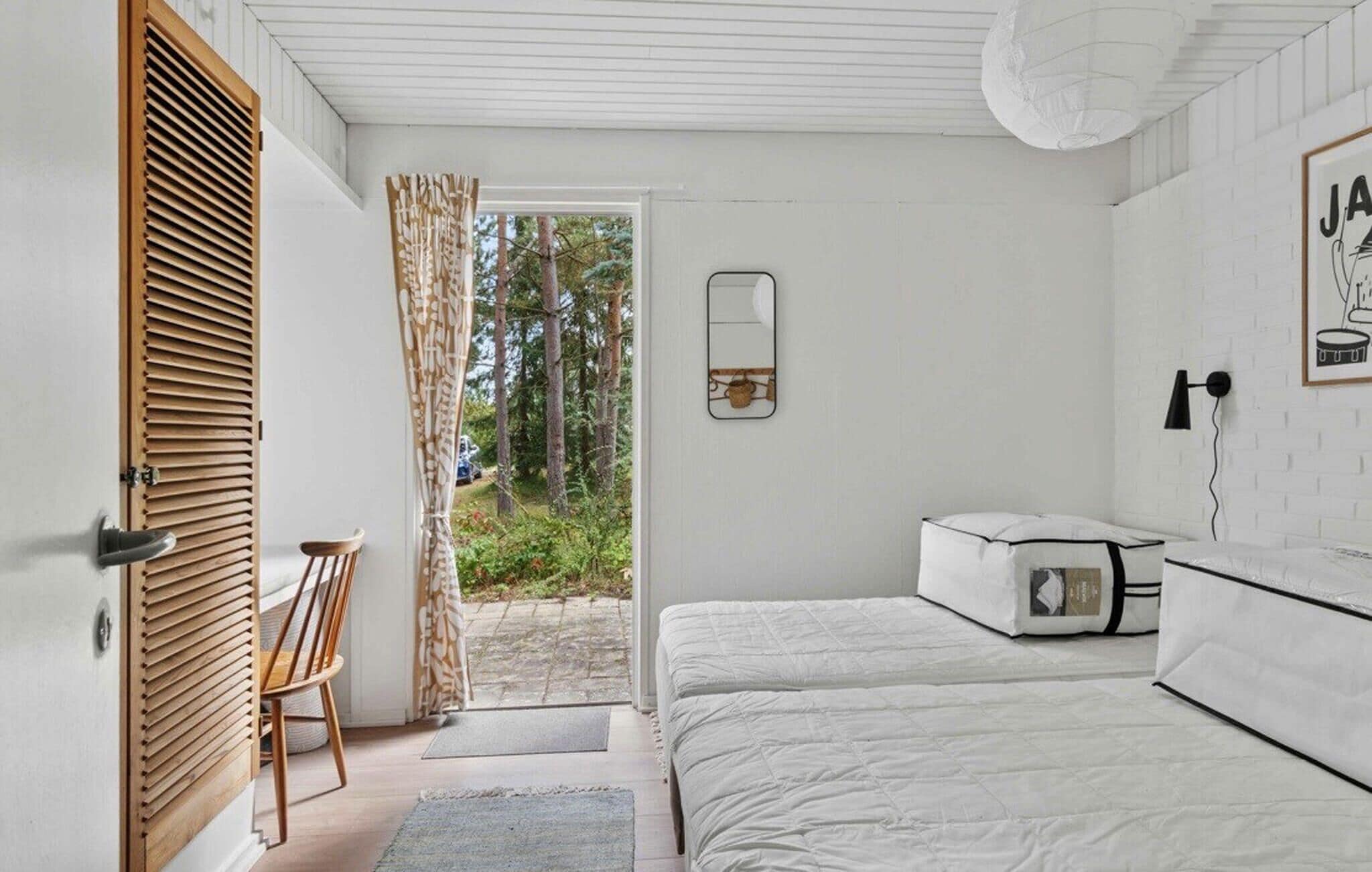 Une chambre à coucher comprenant un lit, une chaise, une table de chevet, un miroir et une porte donnant sur un espace extérieur.