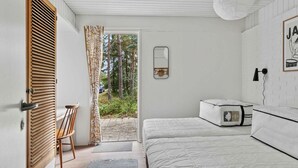 A bedroom with a bed, a chair, a bedside table, a mirror, and a door leading to an outdoor area.