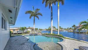 Una piscina de diseño curvo, rodeada de un paseo empedrado y palmeras.