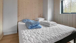 Ein Bett mit weißer Steppdecke, zwei Kissen und einer blauen Decke in einem Zimmer mit holzgetäfelten Wänden und einem Fenster.