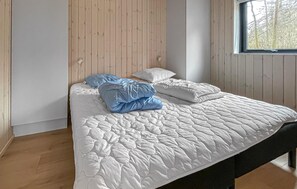 A bed with a white quilted cover, two pillows, and a blue blanket in a room with wooden panel walls and a window. - Awesome home in Vig with WiFi (Vig)